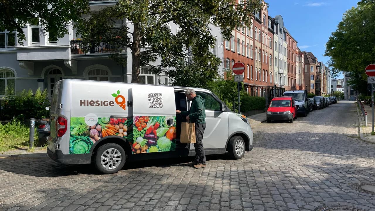 Ein Fahrer nimmt eine Papiertüte aus dem beschrifteten Lieferwagen von Hiesige Höfe in einer Kieler Straße.