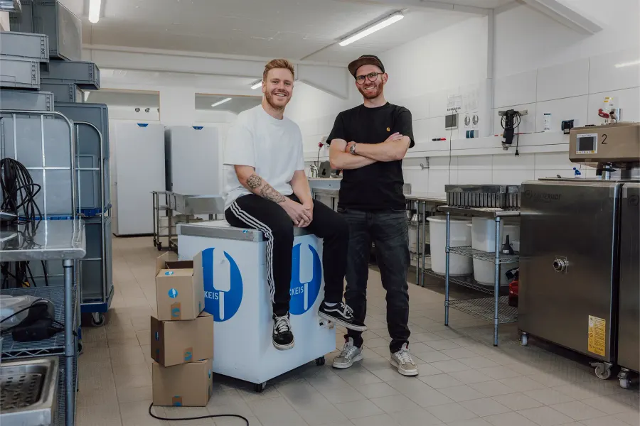 Die beiden Gründer von Packeis Kiel in ihrer Produktion, neben Eistruhe und Eismaschine.